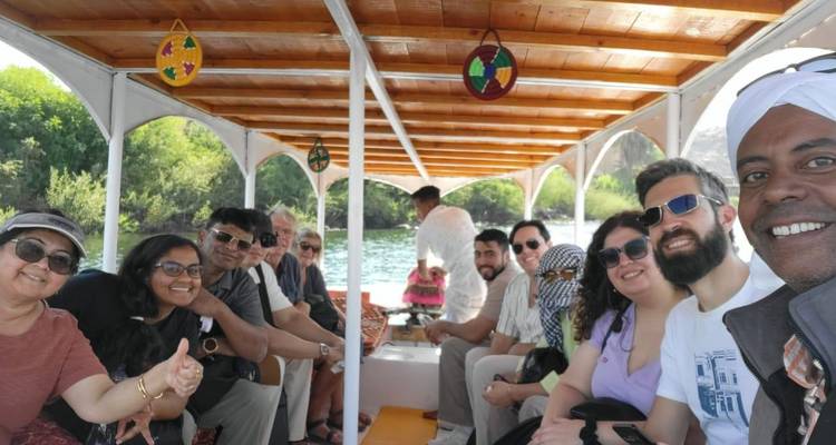 Les touristes sont assis sur des bancs à l'intérieur d'un bateau fluvial couvert qui navigue le long des rives verdoyantes du Nil.