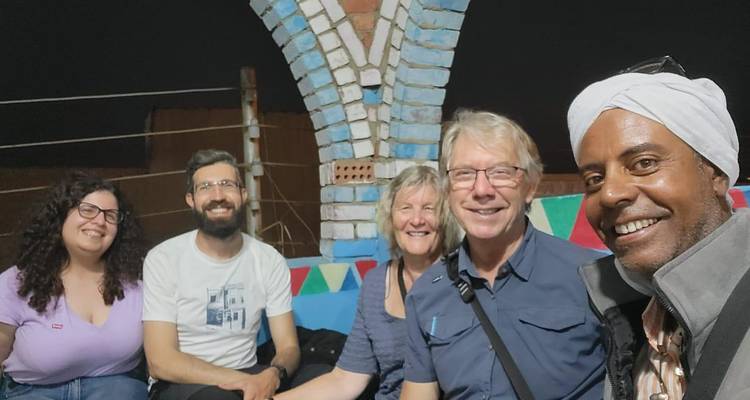 Un petit groupe discute de manière informelle la nuit sous des arches en briques colorées dans une cour nubienne.