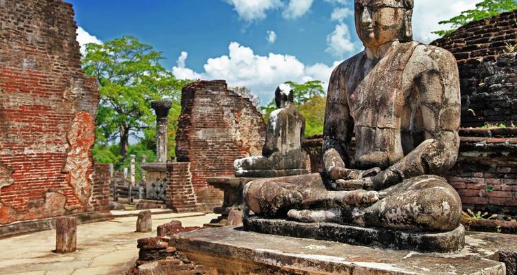Meditatieve stenen Boeddhabeelden in rode bakstenen ruïnes onder een stralend blauwe hemel in Polonnaruwa.