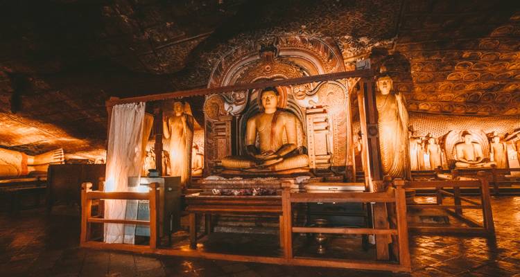 Atmospheric interior of Dambulla Cave Temple with golden Buddha statues illuminated by warm lamplight.