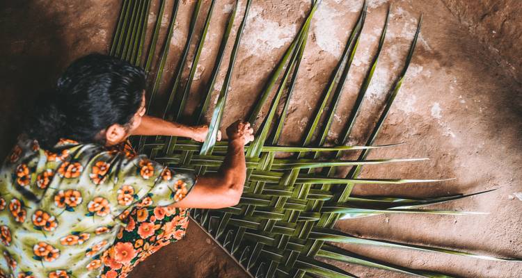 Sri Lankan woman skillfully weaving palm fronds into intricate mats on an earthy floor.