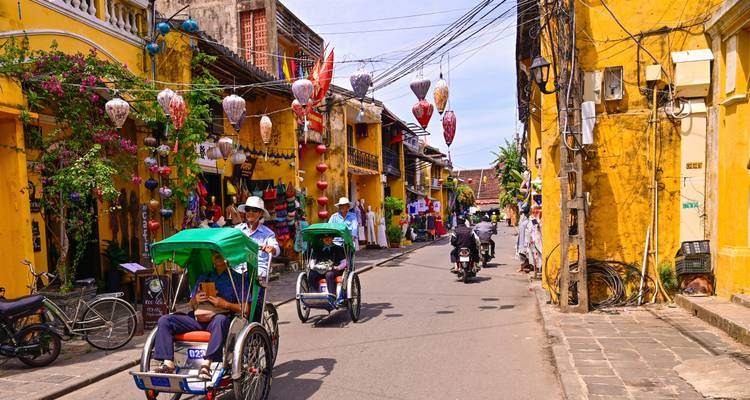 Cyclo drivers pedal through a lantern-lined yellow street in the old town of Hoi An.