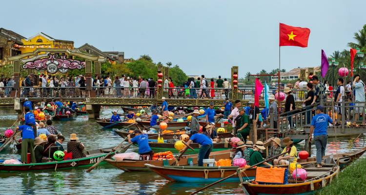 Crowds gather on boats and along a bridge with Vietnamese flags during a river lantern festival.