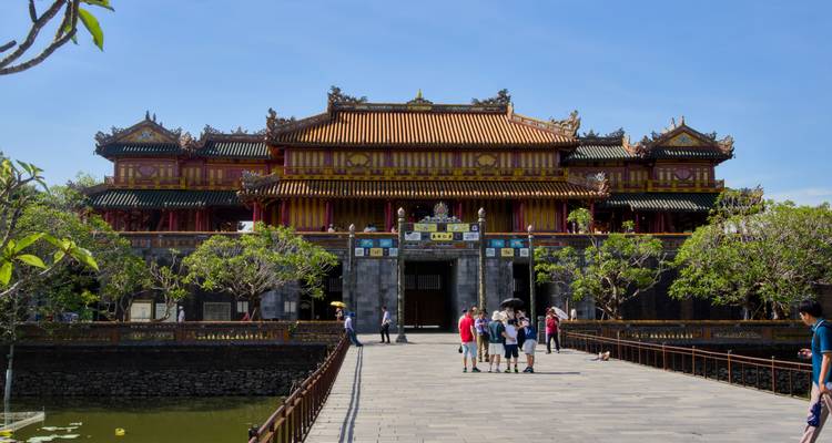 Visitors walk across a stone bridge toward the ornate Ngọ Môn Gate of the Imperial City in Hue.