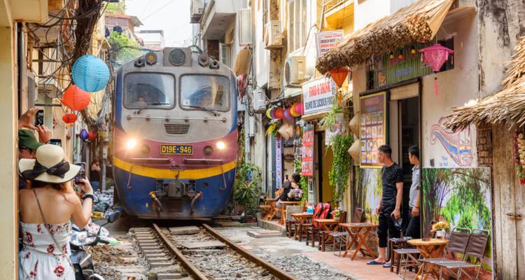 A train squeezes through Hanoi's narrow Train Street as tourists look on from tiny cafés.