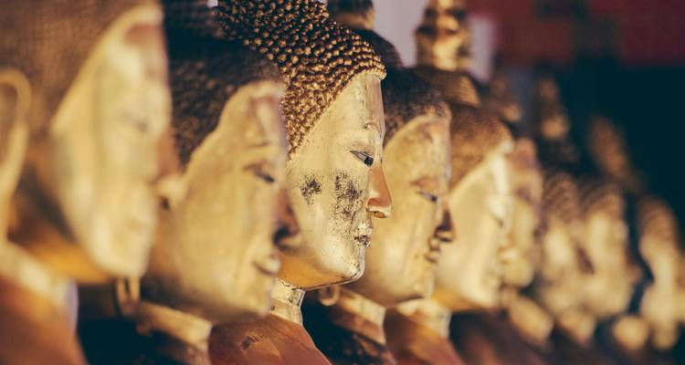Fila de estatuas de Buda doradas de perfil, sus superficies doradas iluminadas suavemente dentro de un templo de Bangkok.