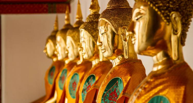 Las estatuas de Buda doradas envueltas en naranja están sentadas en fila dentro de un templo tailandés.