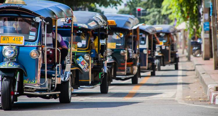 Fila de tuk-tuks coloridos bajando por una calle de Bangkok durante el día.