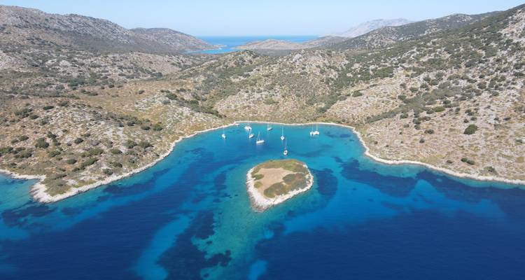Duplicate aerial view of crystal blue cove with yachts moored between rocky hills.