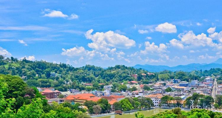 Paisaje urbano brillante de Kandy con tejados naranjas y colinas boscosas alrededor contra un cielo azul.