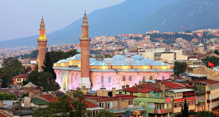 The Grand Mosque (Ulu Cami) of Bursa illuminated at dusk with mountains rising behind the city.