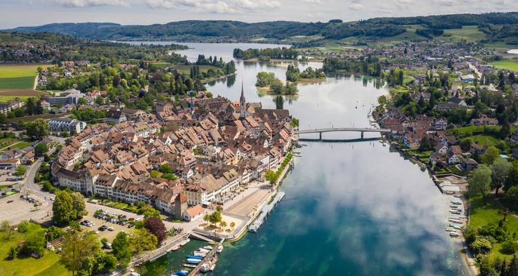 Vue aérienne d'une ville médiévale sur une île fluviale entourée de lacs et de campagnes verdoyantes.