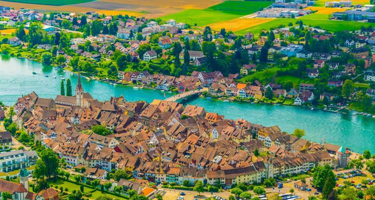 Vue aérienne vivante d'une charmante petite ville médiévale riveraine entourée de terres agricoles verdoyantes.