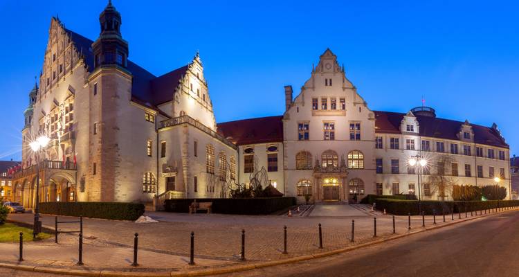 Bâtiment universitaire historique illuminé à Poznań sous un ciel crépusculaire d'un bleu profond