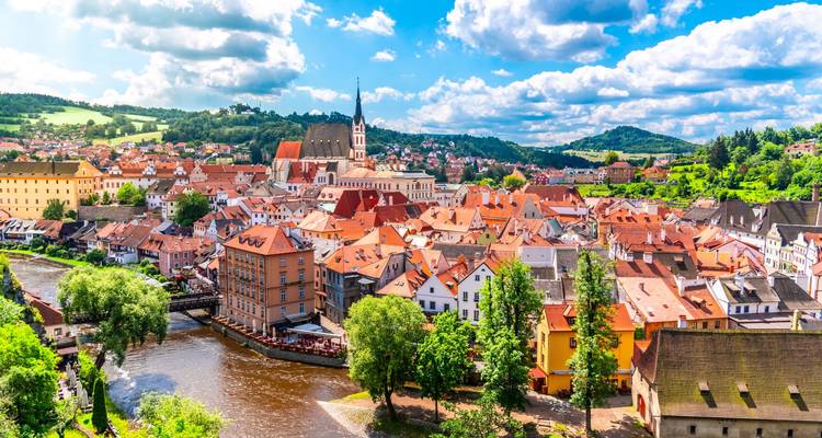 Panorama ensoleillé des toits rouges de Cesky Krumlov s'incurvant le long de la rivière Vltava au milieu de collines ondulantes.