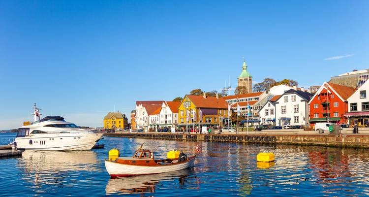 Des bateaux brillants se balancent dans le port de Stavanger devant une toile de fond de bâtiments colorés en bord de mer et d'un ciel bleu dégagé.