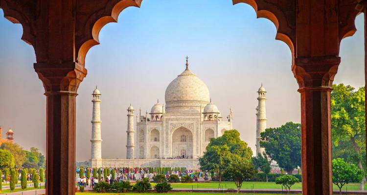 Iconic Taj Mahal framed by ornate archway with visitors on the gardens below.