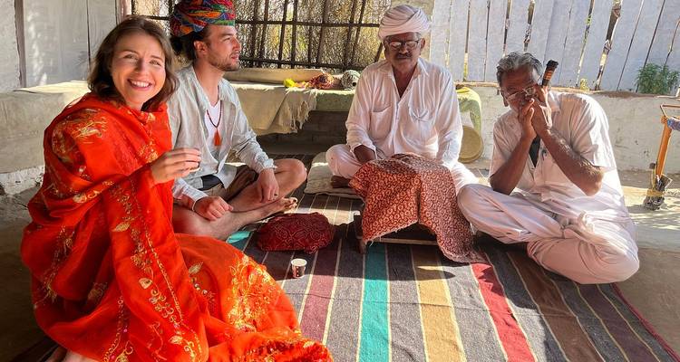 Travelers sit cross-legged with local hosts inside a rural home sharing culture and tea.
