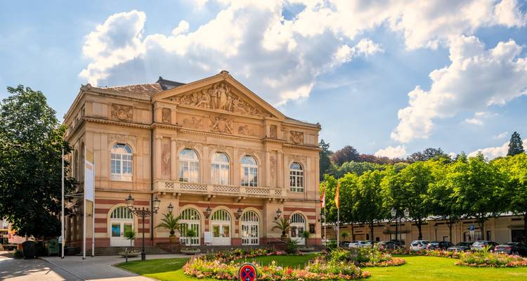 Bâtiment de théâtre élégant de style néoclassique précédé de parterres de fleurs soignés et d'un ciel d'un bleu éclatant