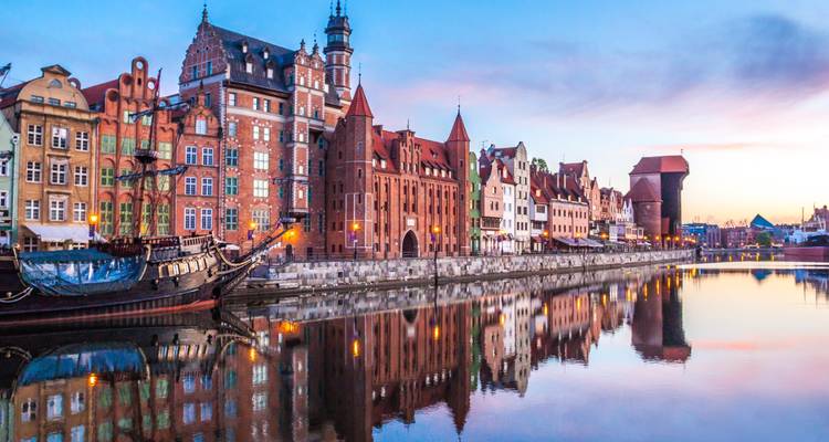 Reflection of Gdańsk’s colorful waterfront houses and medieval crane on calm river at dawn.