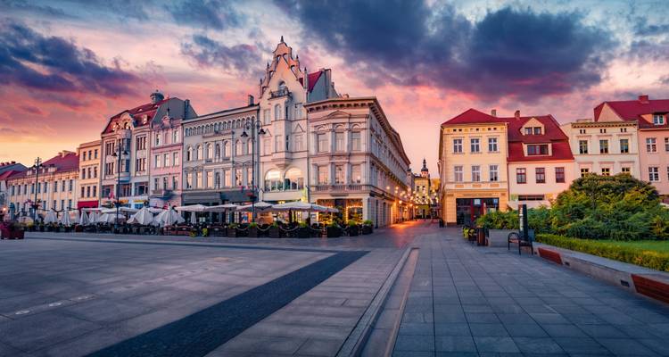 Colorful historic facades border a spacious European market square under a vivid sunset sky.