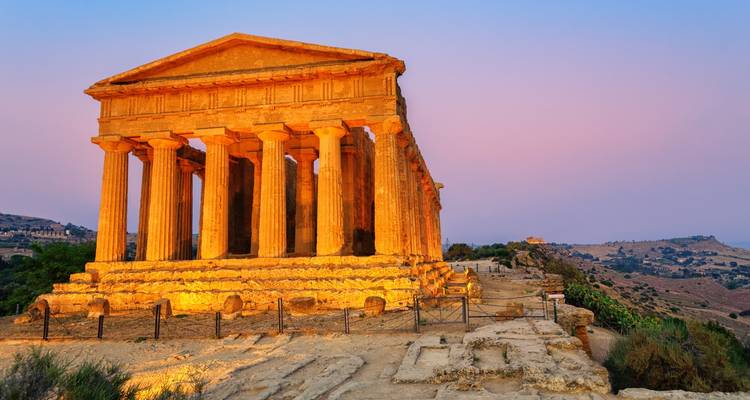 Temple illuminé de la Concorde dans la Vallée des Temples d'Agrigente brillant sous un ciel crépusculaire aux teintes pastel.