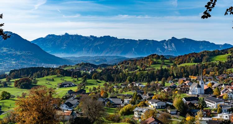 Village autrichien coloré niché parmi des collines verdoyantes ondulantes et des chaînes alpines lointaines.