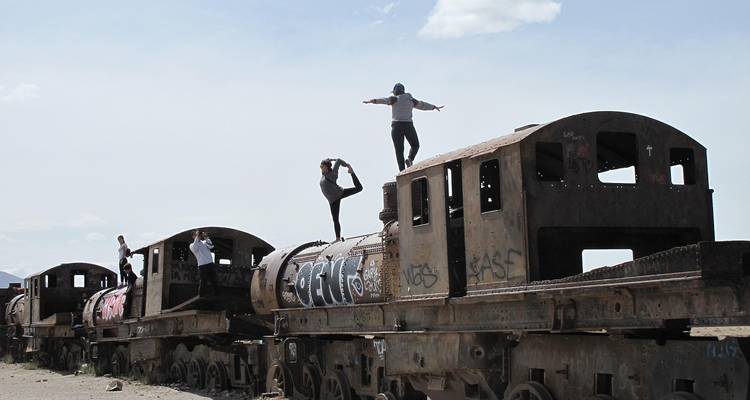 Los viajeros se equilibran y posan sobre vagones de tren abandonados cubiertos de graffiti.