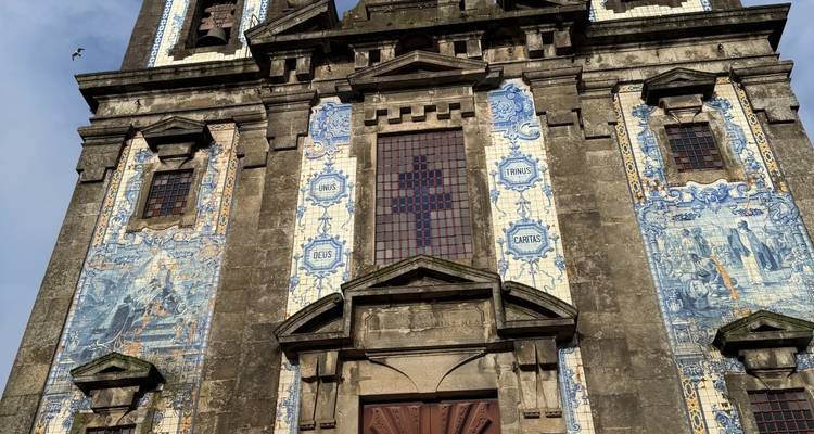 Detalle de la torre de la iglesia revestida de azulejos con cruz contra el cielo azul, un pequeño pájaro volando.