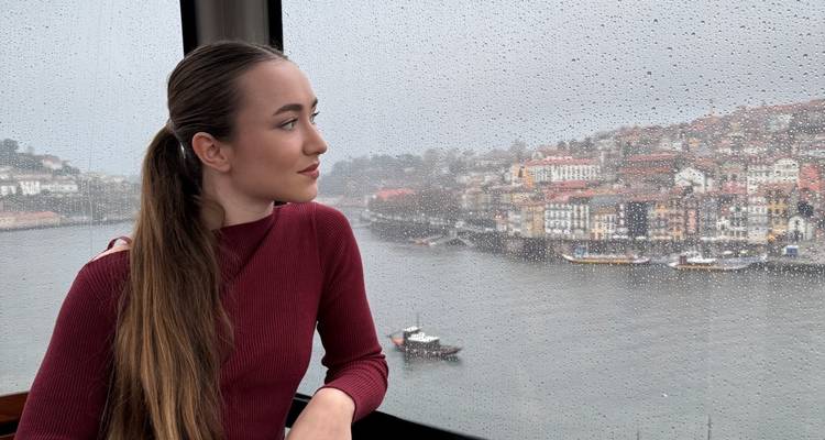 Mujer mirando por la ventana de la góndola salpicada de lluvia hacia la orilla del río Oporto borrosa abajo.