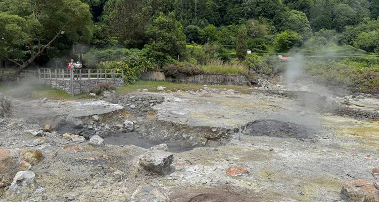 Respiraderos geotermales humeantes y terreno árido en un campo de fumarolas con visitantes observando desde una plataforma de madera.