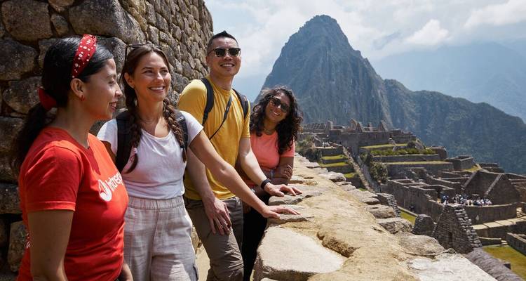 Les voyageurs sourient en admirant les terrasses de pierre emblématiques et le sommet du Machu Picchu sous un ciel dégagé.