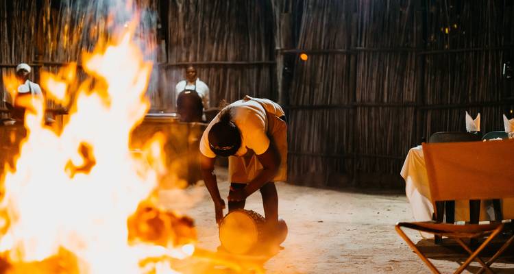 Un artiste se penche au-dessus d'un tambour près d'un feu de camp rugissant lors d'un spectacle culturel nocturne