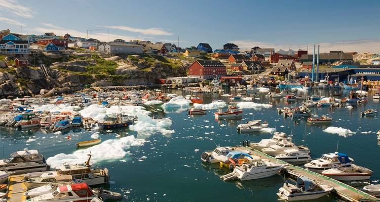 Farbenfroher grönländischer Hafen mit Fischerbooten und schwimmenden Eisbrocken an einem sonnigen Sommertag.
