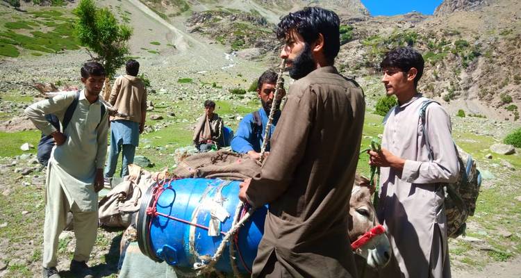 Local porters with a laden donkey prepare gear in a rocky high-altitude pasture.