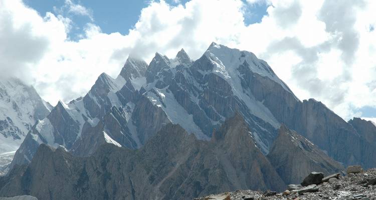 Dramatic serrated granite peaks capped with fresh snow thrust into a partly cloudy sky.