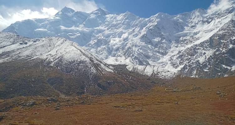 Snow-capped mountain massif towering above a rust-colored alpine meadow under clear skies.