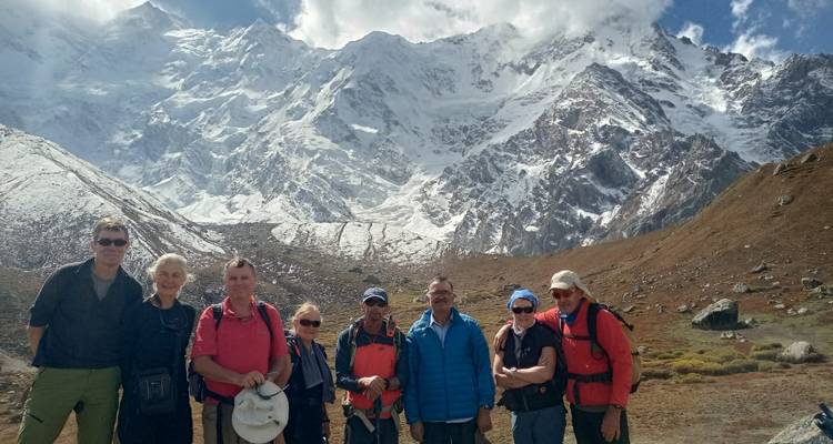 Group of trekkers posing with a dramatic snow-covered Himalayan peak behind them.