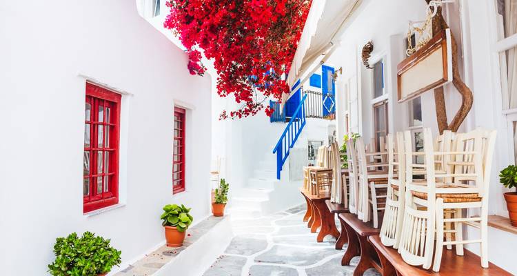 Ruelle blanchie à la chaux charmante avec du bougainvillier rouge vif et des chaises de café empilées à Mykonos.