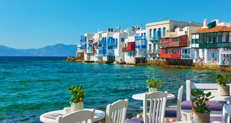 Tables de café en bord de mer avec des plantes en pots face au front de mer coloré de la Petite Venise de Mykonos.