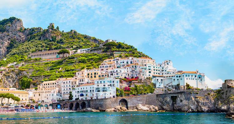 Les bâtiments colorés et empilés de la ville d'Amalfi s'élevant au-dessus d'une eau turquoise et de falaises rocheuses.