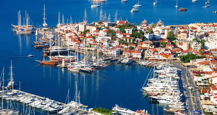 Colorful panorama of Marmaris marina filled with yachts and historic castle walls beside sapphire water.