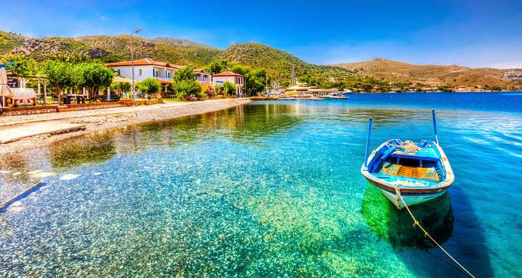 Crystal-clear pebbled shoreline with a lone blue wooden boat floating on transparent turquoise water.