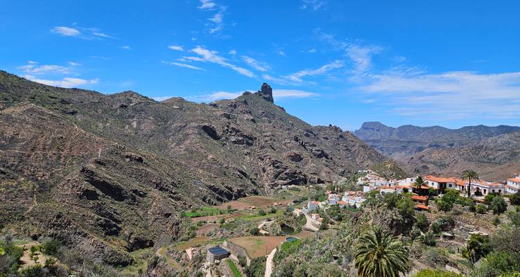 Village perché sur le flanc d'une colline avec des palmiers en contrebas et le Roque Bentayga se dressant majestueusement à l'horizon.