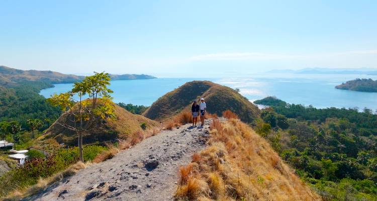 A coastal trail on a golden ridge with hikers and sweeping views of turquoise bays and islands.
