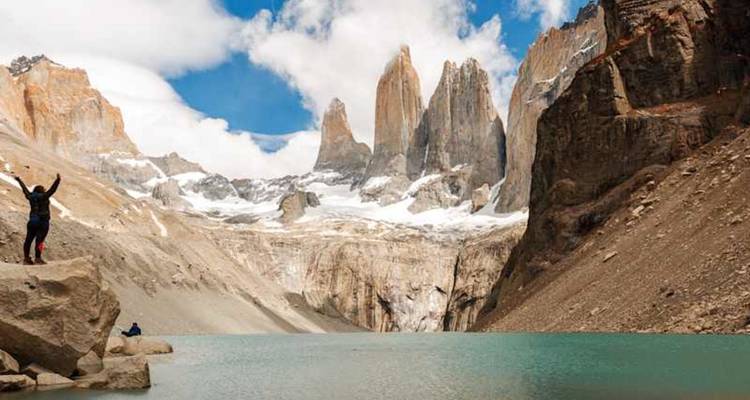 Un excursionista triunfante levanta los brazos junto a la laguna turquesa en la base de los icónicos picos de granito de Torres del Paine.