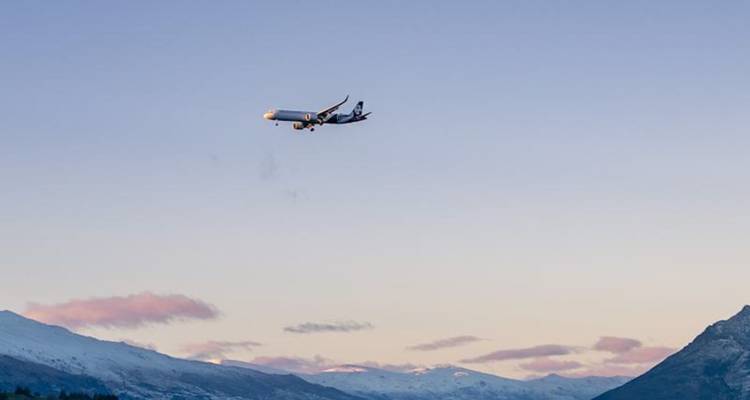 Avion commercial descendant au-dessus d'une chaîne de montagnes enneigées dans la lumière douce du soir.