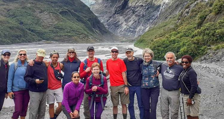 Groupe de randonneurs souriants posant dans une vallée glaciaire spectaculaire entourée de montagnes vertes aux pentes abruptes.