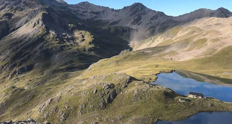 Bassin montagneux élevé avec un lac alpin aux eaux réfléchissantes et des crêtes escarpées sous un ciel dégagé.