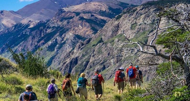 Un groupe de trekking suit un sentier de crête herbeux au-dessus de parois rocheuses abruptes et de paysages sauvages de Patagonie.
